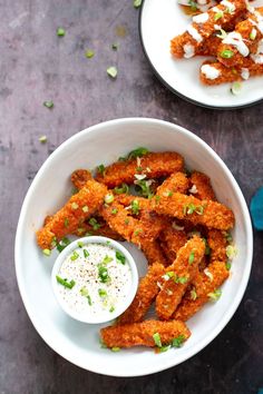 a bowl filled with fried food next to another bowl full of dipping sauce and green onions