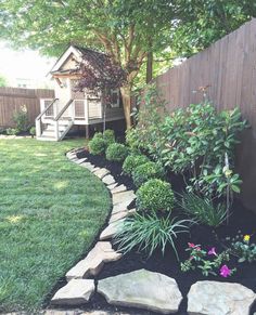 a garden with rocks and flowers in the grass near a fenced in backyard area