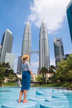 a woman standing on the edge of a swimming pool in front of tall buildings