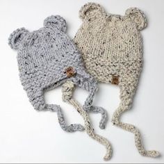 two knitted hats are laying next to each other on a white surface, one is grey and the other is light gray