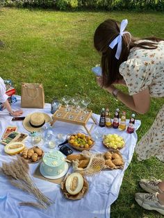 two women sitting at a picnic table with food and drinks on the grass, one holding a wine glass in her hand