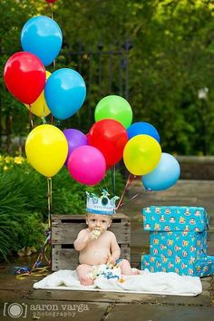 a baby wearing a crown sitting on a blanket with balloons