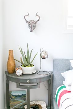 a small table with some plants on it and a clock in the corner next to it