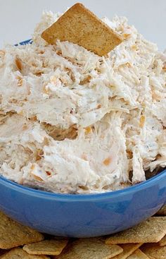 a blue bowl filled with chicken salad next to a cracker on top of it