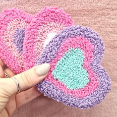 a hand holding three crocheted coasters on top of a pink blanket next to a person's finger