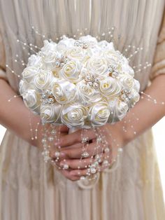 a bridal holding a bouquet of white roses and pearls in it's hands