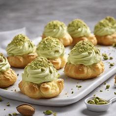 there are many small pastries with green toppings on the tray next to nuts