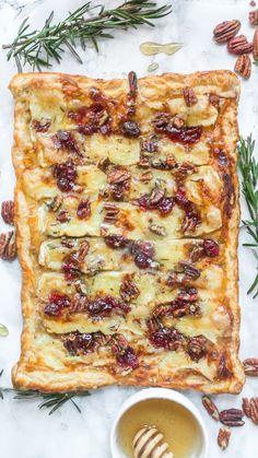 a square pastry with nuts and cranberries next to a cup of tea on a marble surface