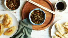 two white plates with food on them next to some chopsticks and sauce in bowls