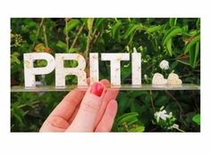 a person holding up the word prit in front of some bushes and trees with white flowers