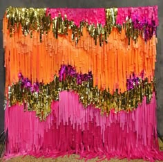 an orange, pink and gold streamer backdrop on a metal stand in front of a gray wall