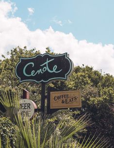 a sign for a coffee shop and eatery in front of some trees with clouds