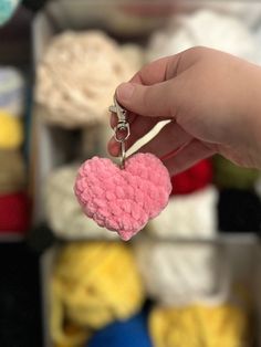 a hand holding a pink heart shaped keychain in front of some crochet balls