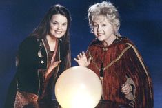 two women standing next to each other in front of a white ball on a table