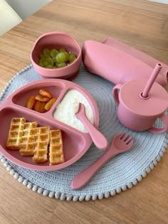 a pink plate topped with waffles, fruit and yogurt next to a fork