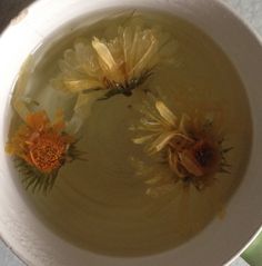 three yellow flowers floating in water in a white bowl on a counter top with other items