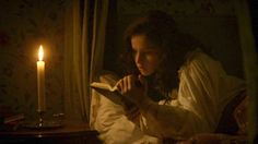 a woman sitting in bed reading a book next to a candle