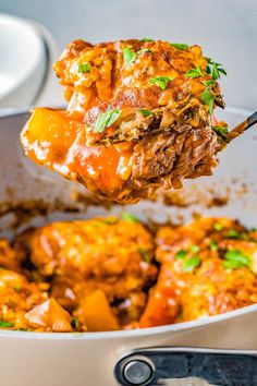 a spoon full of meat and vegetables being lifted from a casserole dish