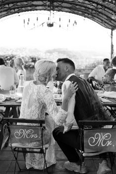 a man and woman kissing each other at an outdoor wedding reception in black and white