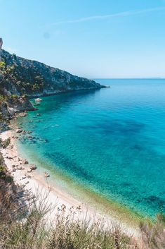 the beach is clear and blue with white sand on it's shore, as well as green vegetation