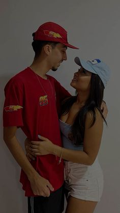 a man and woman standing next to each other in front of a white wall wearing baseball caps