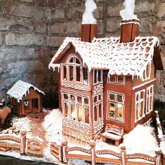 a gingerbread house is on display in front of a stone wall with snow around it