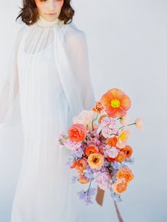 a woman holding a bouquet of flowers in front of her face and wearing a white dress