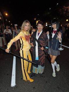 three women dressed up in costumes posing for the camera at an outdoor halloween event with people standing behind them