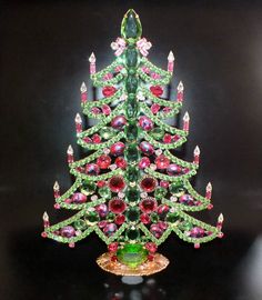 a green and red christmas tree made out of glass beads on a black surface with candles in the background