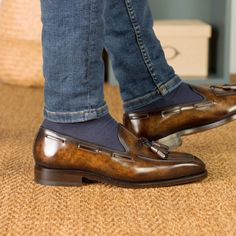 a person wearing blue jeans and brown loafers standing on a carpeted floor with their feet in the air