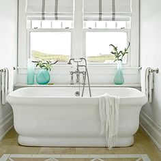 a white bath tub sitting under a window next to two vases filled with flowers