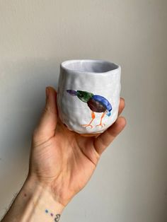 a hand holding a small cup with two birds painted on it's sides and bottom