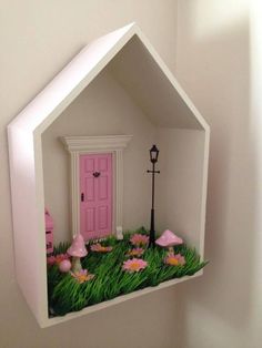 a pink door is in the shape of a house with green grass and flowers on it