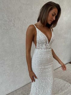 a woman in a white wedding dress standing next to a wall and looking down at the floor