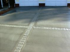 an empty driveway in front of a house with two garage doors on one side and another door on the other