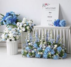 blue and white flowers in vases next to a welcome sign