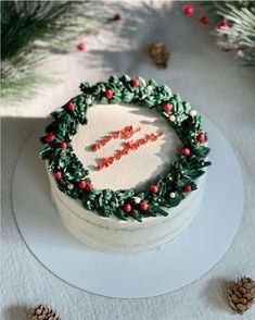 a cake decorated with pine cones and red berries on a white platter surrounded by pine cones