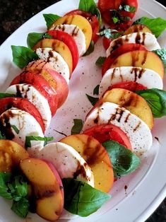 a white plate topped with sliced peaches and mozzarella on top of green leaves