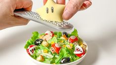 a person holding a remote control over a bowl of salad with a toy house on it