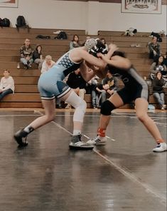 two women wrestling in a gym with spectators watching