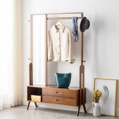 a coat rack with clothes and hat on it next to a mirror, potted plant and framed photograph