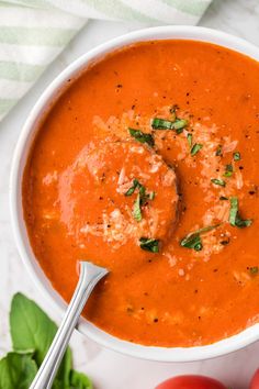 a bowl of tomato soup with meatballs and basil on the side next to tomatoes