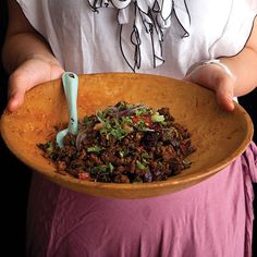 a person holding a wooden bowl filled with food and a blue spatula in their hands