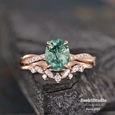 an engagement ring with a green stone surrounded by white diamonds on top of a rock