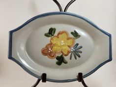 a white and blue plate with flowers painted on the side is hanging from a metal holder