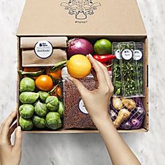 a person reaching for an orange in a box filled with vegetables