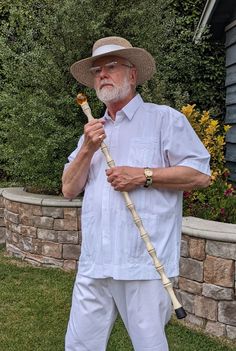 an older man in white holding a stick and wearing a straw hat, standing on the grass