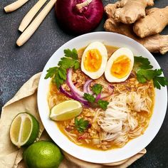 a bowl of ramen with hard boiled eggs, onions and cilantro on the side