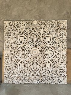 an intricately carved wooden panel on display in a room with concrete walls and cement flooring