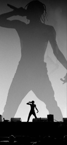 a man standing on top of a stage in front of a giant shadow behind him